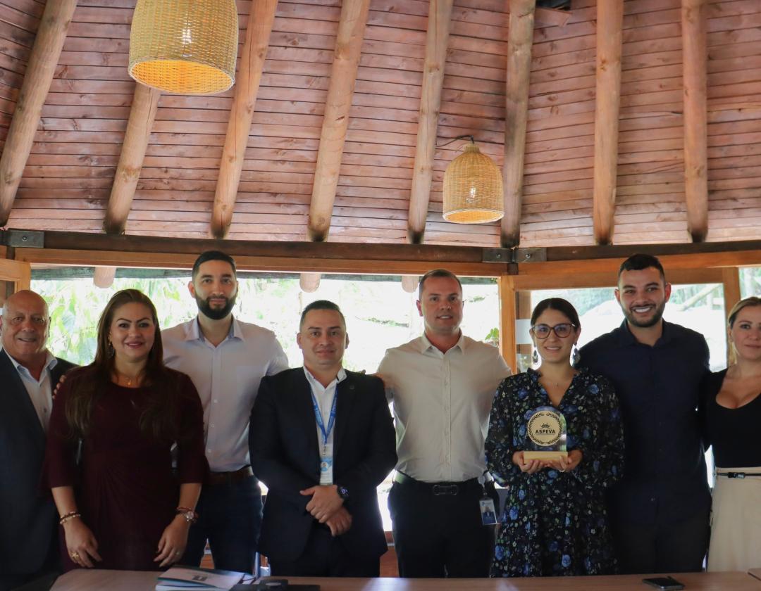 En la foto aparecen 10 personas posando en un espacio tipo kiosco de madera, iluminado con lámparas colgantes que aportan calidez al lugar.

Están ubicadas en fila frente a una mesa y visten de manera formal y semiformal. En el centro, una mujer sostiene un reconocimiento con la inscripción ASPEVA, lo que indica que se trató de un acto de entrega o reconocimiento institucional.

La fotografía refleja un ambiente de camaradería, trabajo conjunto y celebración de logros colectivos.